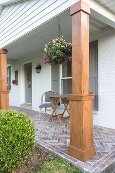 a porch with chairs, table and potted plants hanging from the side of it