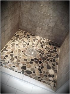 there is a shower with stones on the floor and walls in this bathroom, as well as a drain