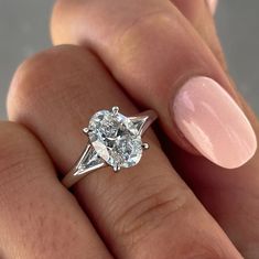 a woman's hand holding a ring with a diamond on it and a pink manicure