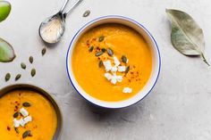 there is a bowl of carrot soup with cream on the top and two spoons next to it