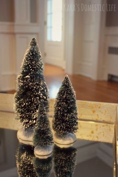 two small christmas trees sitting on top of a glass table next to a mirror in a room