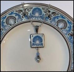 a blue and white plate with a silver necklace hanging from it's center piece