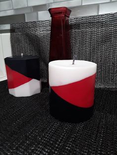 two candles sitting on top of a table next to a red vase and black container