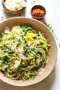 a bowl filled with pasta and vegetables on top of a white table next to bowls of seasoning