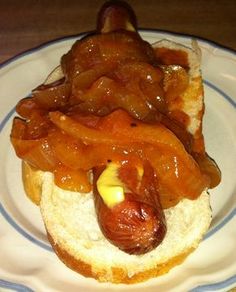 a hot dog on a bun with onions and mustard in it sitting on a plate