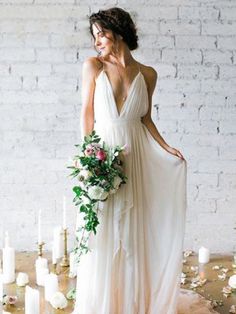 a woman in a white dress standing next to candles with flowers and greenery on the floor