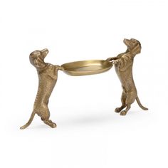 two small brass monkeys playing with a metal bowl on a white background in the shape of a cat and dog