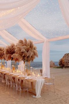 a long table set up on the beach with candles and pamolite centerpieces