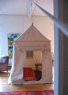 a white tent sitting on top of a hard wood floor next to a red rug