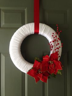 a white yarn wreath with poinsettis and red ribbon hanging on a door