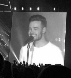 a black and white photo of a smiling man on a large screen at a concert