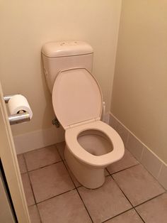 a white toilet sitting in a bathroom next to a roll of toilet paper on the wall