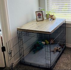 a dog crate with two puppies in it next to a wooden table and window