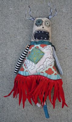 a stuffed animal with red fringes on it's head and eyes sitting on the ground