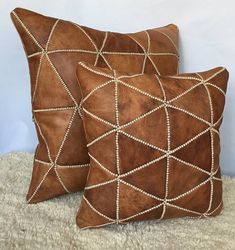 two brown leather pillows sitting on top of a carpeted floor next to each other