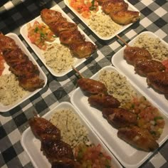 several trays filled with chicken and rice covered skewers on a checkered table cloth