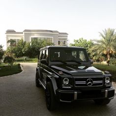 a black mercedes g - class parked in front of a large house with palm trees