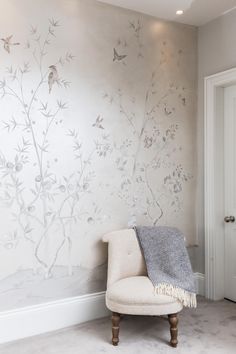 a white chair sitting in front of a wall with birds on it and branches painted on it