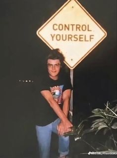 a young man leaning against a control yourself sign in front of a potted plant