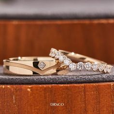 two gold wedding rings with diamonds sitting on top of a wooden box next to each other