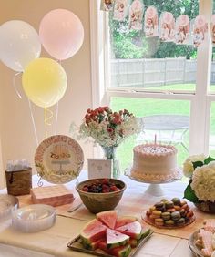 a table with cake, watermelon slices and other desserts on it in front of a window