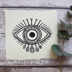 an eye drawn on top of a piece of paper next to a plant with leaves