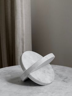 a white marble table with a circular object on it's top and a curtain in the background