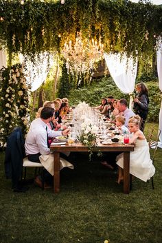 a group of people sitting at a table with food and drinks on it in the grass