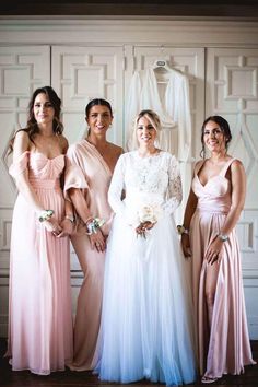 four bridesmaids pose for a photo in front of a white wall wearing pink and blue gowns