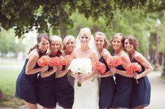 a group of women standing next to each other in front of trees and flowers on the sidewalk