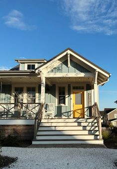 a white house with yellow door and steps leading up to the front porch on a sunny day