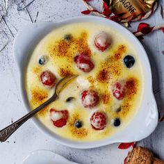 a white bowl filled with pudding and fruit on top of a table next to two spoons