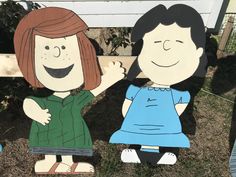 two paper cutouts of people sitting on the ground in front of a fence with grass