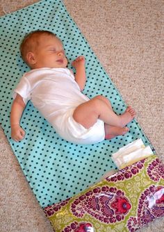 a baby laying on top of a blue mat next to a green and white bag