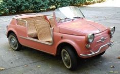 an old pink car parked on the side of the road in front of some bushes