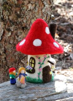 a small red mushroom house sitting next to a tree with two gnomes on it