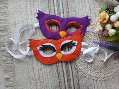 two colorful masks sitting on top of a table next to some flowers and laces