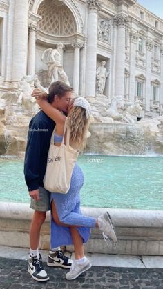 a man and woman kissing in front of a fountain