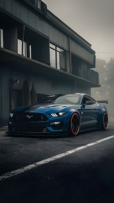 a blue mustang parked in front of a tall building on a foggy day with orange rims