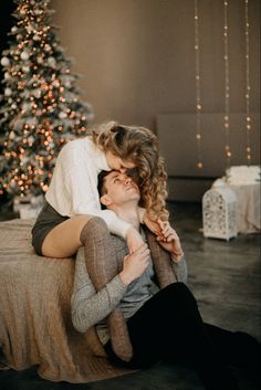 a man and woman cuddle in front of a christmas tree