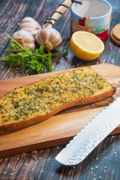 a knife on a cutting board next to garlic and lemon