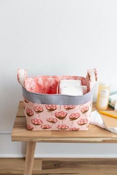 a pink and gray basket sitting on top of a wooden table next to a white wall