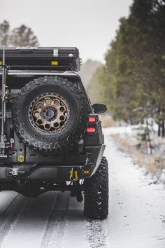 a truck driving down a snowy road with trees in the background and snow on the ground