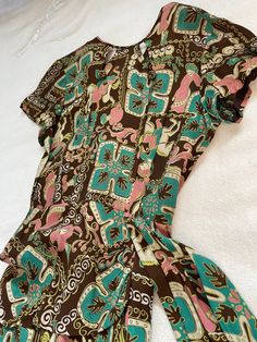 "Amazing 1940s dress with the coolest novelty print chocolate brown with pink and turquoise genie figures Both on horses abs playing instruments. Cold rayon fabric with no holes, spots or odors. Amazing condition! The dress has a crew neck with two peepholes in the front and finished off with a gold button. There are pleats down the bustling which stop at the waist on the right side and continue past the waist on the left side into a 14\" sash as pictured. The dress has a zipper in the back whic Vintage Printed Brown Dress, Vintage Brown Printed Dress, Brown Vintage Printed Dress, Vintage 40s Dress, Dress Peplum, 40s Dress, Tooled Leather Purse, Beaded Sweater, 1940s Dresses