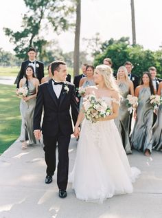 a bride and groom walking down the sidewalk with their bridal party in the background