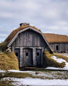 an old barn with snow on the ground and grass growing on it's roof