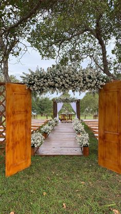 an outdoor wedding ceremony with wooden doors and flowers on the aisle, surrounded by greenery