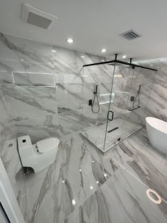 a bathroom with marble walls and flooring has a white bathtub, toilet, shower head, and standup shower