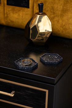 two gold rings are sitting on top of a black table next to a golden vase