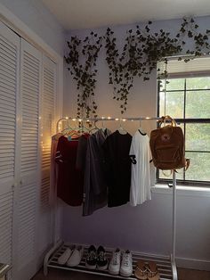 clothes are hanging on a rack in front of a window with lights strung from it